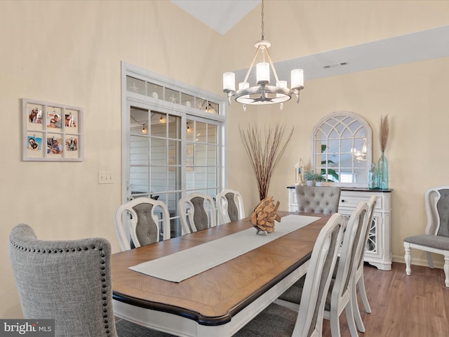 dining space featuring visible vents, baseboards, vaulted ceiling, an inviting chandelier, and wood finished floors