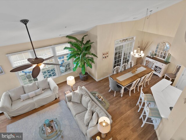 living area featuring ceiling fan with notable chandelier, baseboards, lofted ceiling, and wood finished floors