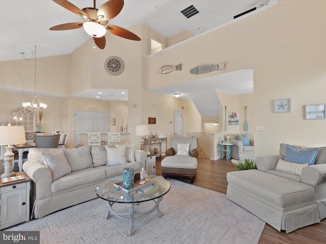 living area with ceiling fan with notable chandelier, wood finished floors, visible vents, and high vaulted ceiling