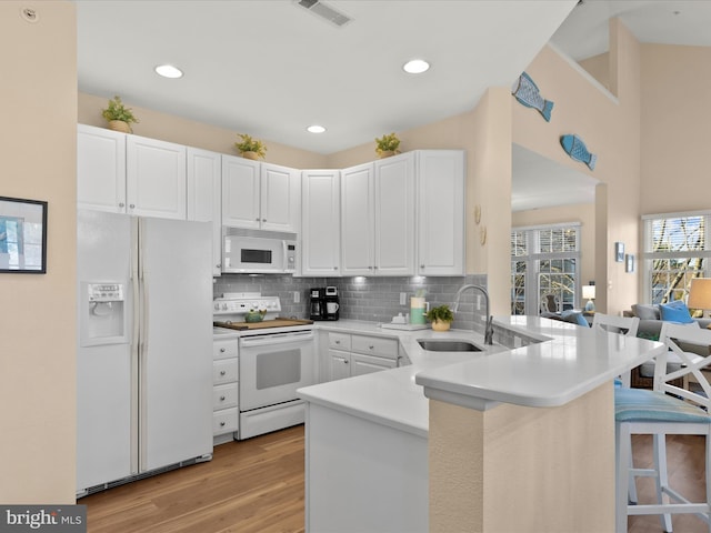 kitchen featuring white appliances, visible vents, a peninsula, a sink, and a kitchen breakfast bar