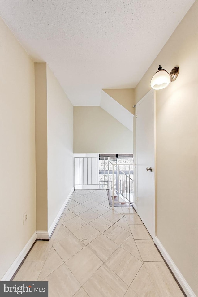 hall featuring baseboards, a textured ceiling, and vaulted ceiling