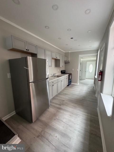 kitchen with black electric range, light countertops, light wood-style flooring, freestanding refrigerator, and a sink