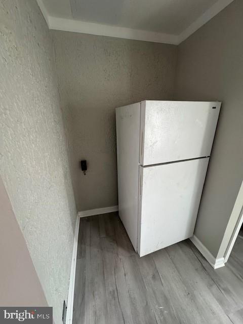 kitchen with a textured wall, light wood-style flooring, baseboards, and freestanding refrigerator