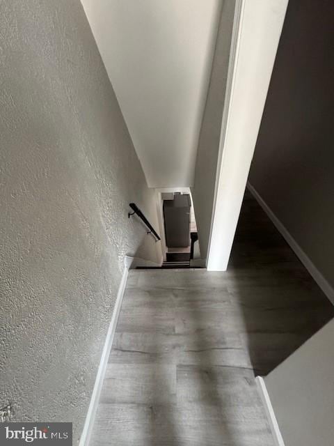 staircase with a textured wall, wood finished floors, and baseboards