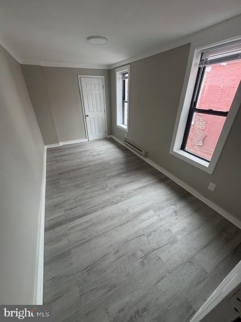 empty room featuring baseboards, crown molding, a baseboard heating unit, and wood finished floors