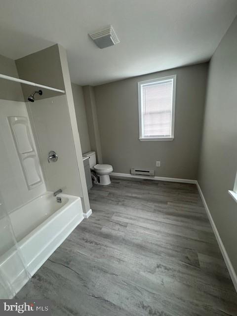 bathroom with baseboards, bathing tub / shower combination, toilet, a baseboard radiator, and wood finished floors