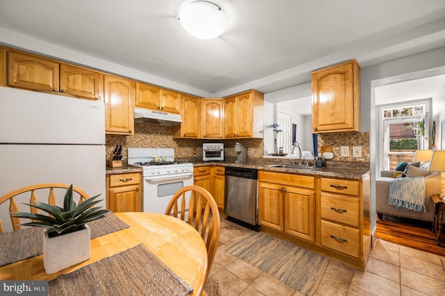 kitchen featuring tasteful backsplash, dark countertops, a sink, white appliances, and under cabinet range hood