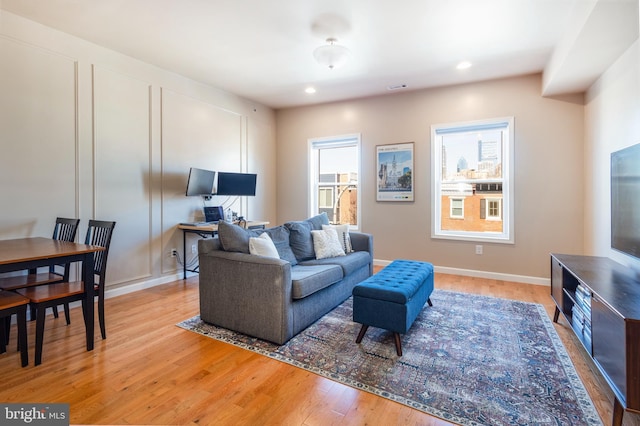 living room featuring recessed lighting, visible vents, a decorative wall, light wood-type flooring, and baseboards