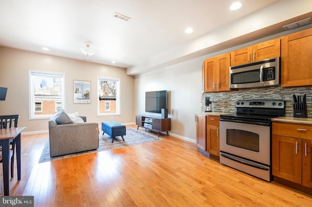 kitchen with visible vents, brown cabinetry, stainless steel appliances, light wood-type flooring, and backsplash