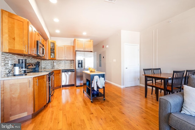 kitchen featuring light wood finished floors, glass insert cabinets, appliances with stainless steel finishes, light countertops, and backsplash