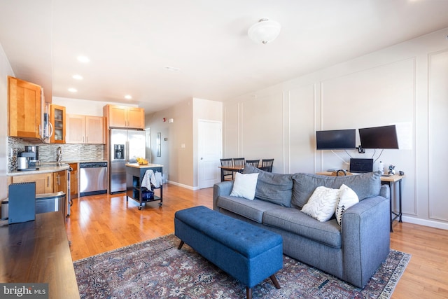 living room featuring light wood-type flooring, a decorative wall, baseboards, and recessed lighting