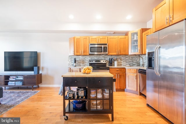 kitchen with light wood-style flooring, glass insert cabinets, backsplash, stainless steel appliances, and a sink