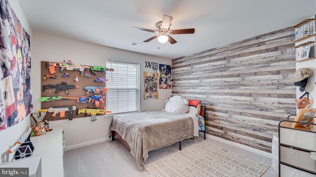 bedroom with wooden walls, visible vents, a ceiling fan, an accent wall, and carpet