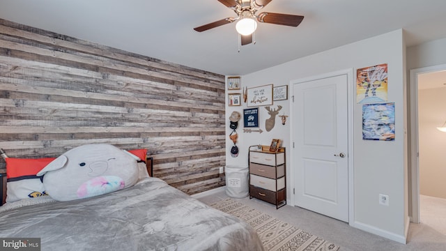 bedroom featuring ceiling fan, an accent wall, wood walls, carpet flooring, and baseboards