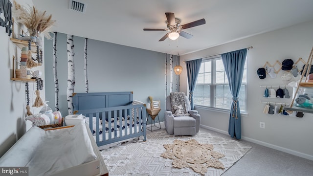 carpeted bedroom featuring a ceiling fan, a nursery area, visible vents, and baseboards