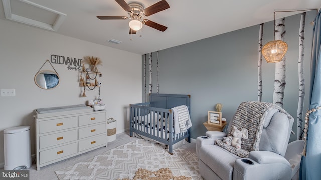 bedroom with light carpet, a crib, attic access, visible vents, and ceiling fan