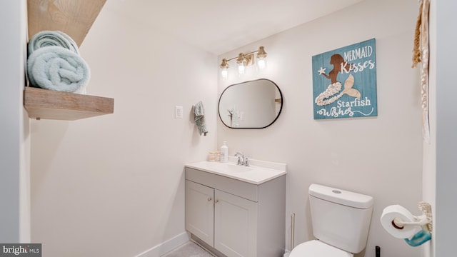 half bath with baseboards, vanity, and toilet