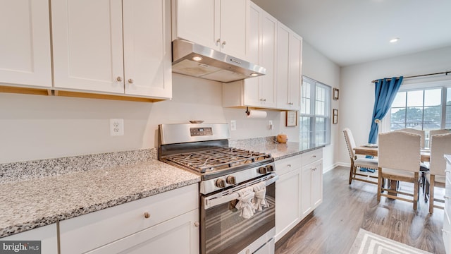 kitchen featuring white cabinets, stainless steel range with gas stovetop, light stone countertops, light wood-type flooring, and under cabinet range hood