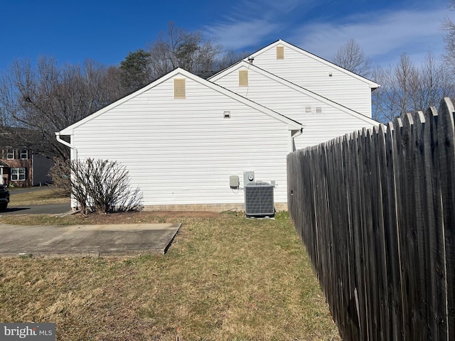 view of side of property featuring central AC, fence, and a lawn