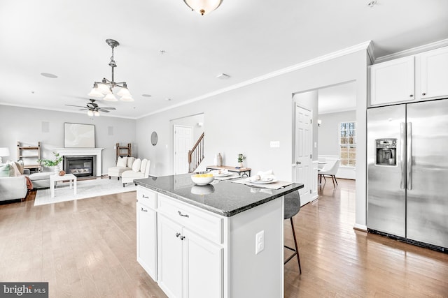 kitchen with stainless steel fridge, light wood-style flooring, a kitchen island, dark stone countertops, and a glass covered fireplace