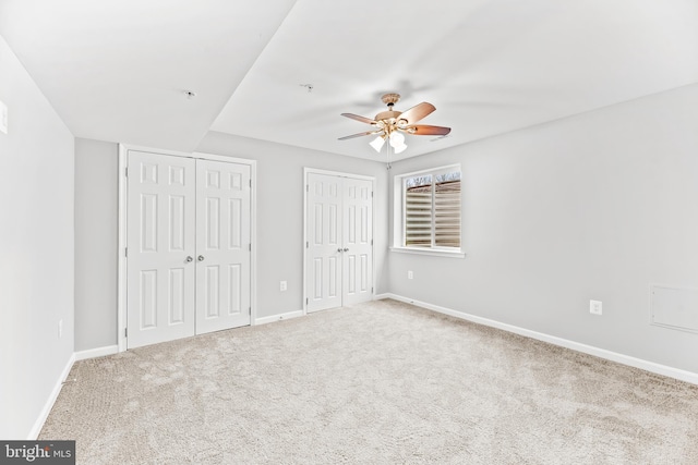 unfurnished bedroom with a ceiling fan, baseboards, two closets, and carpet flooring