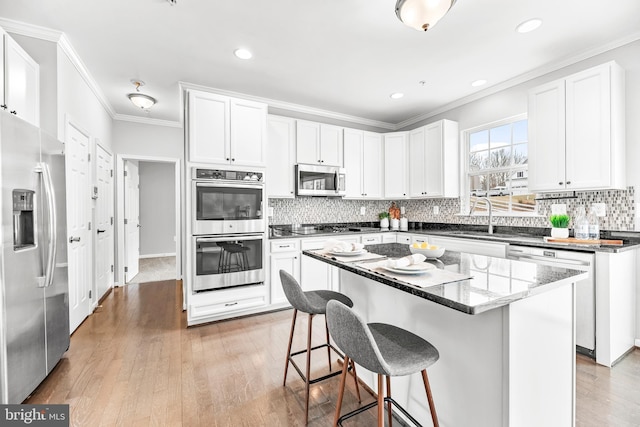 kitchen featuring crown molding, stainless steel appliances, light wood-type flooring, and a kitchen breakfast bar