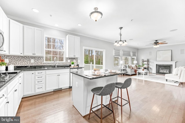 kitchen with a glass covered fireplace, dark countertops, a breakfast bar area, crown molding, and a sink