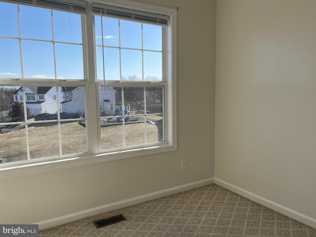 spare room with plenty of natural light, carpet, visible vents, and baseboards