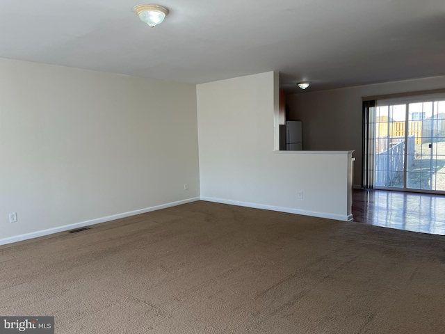 unfurnished room with dark colored carpet, visible vents, and baseboards