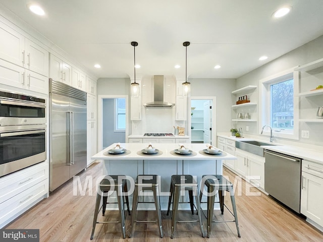 kitchen featuring a breakfast bar area, stainless steel appliances, open shelves, a sink, and wall chimney exhaust hood