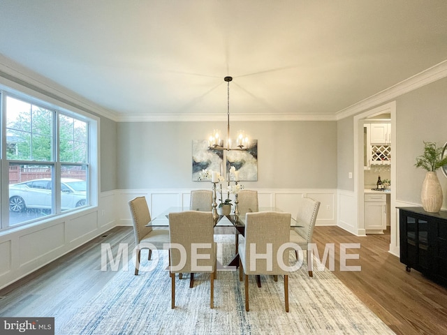 dining area featuring ornamental molding, wainscoting, a notable chandelier, and wood finished floors