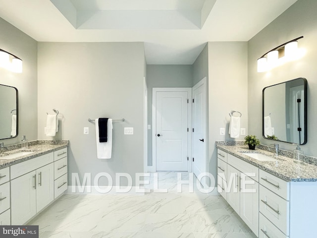 bathroom featuring marble finish floor, a tray ceiling, two vanities, and a sink