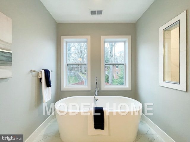 full bathroom with marble finish floor, visible vents, a freestanding tub, and baseboards