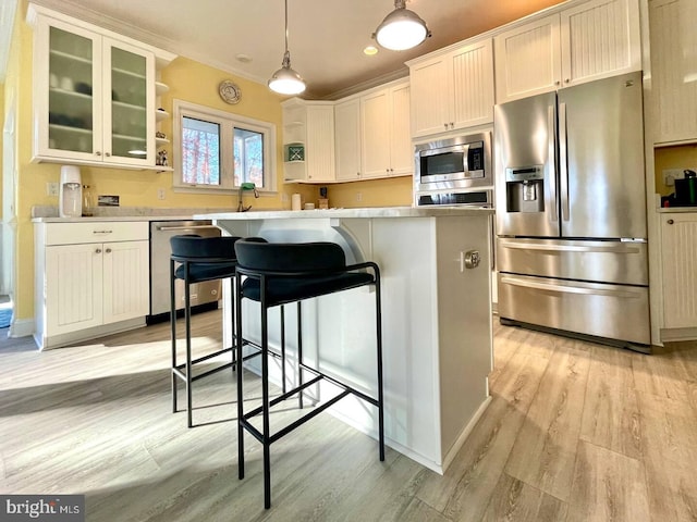 kitchen featuring stainless steel appliances, light wood-style floors, light countertops, a center island, and glass insert cabinets