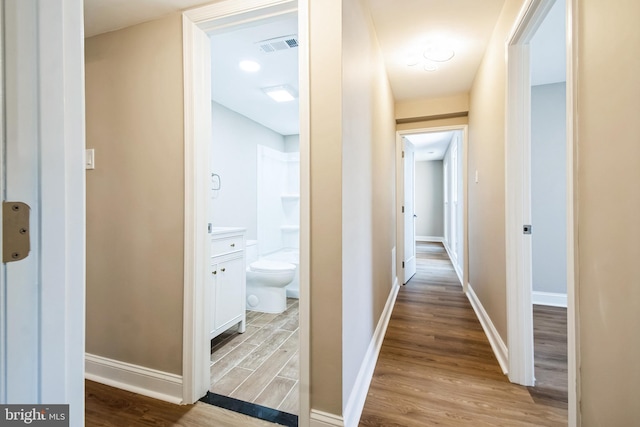 hallway with wood finished floors, visible vents, and baseboards