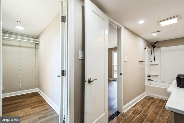 full bath with baseboards, visible vents, bathing tub / shower combination, wood finished floors, and vanity