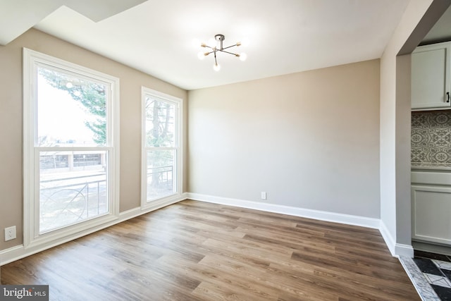 unfurnished dining area with a notable chandelier, wood finished floors, and baseboards