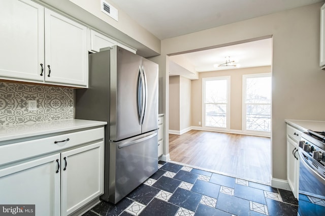 kitchen featuring stainless steel appliances, backsplash, white cabinetry, and stone tile floors