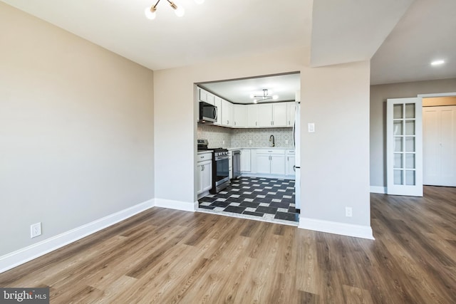 kitchen with baseboards, stainless steel gas stove, decorative backsplash, and white cabinets