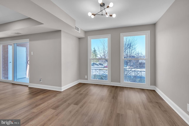 unfurnished dining area featuring a notable chandelier, baseboards, visible vents, and wood finished floors