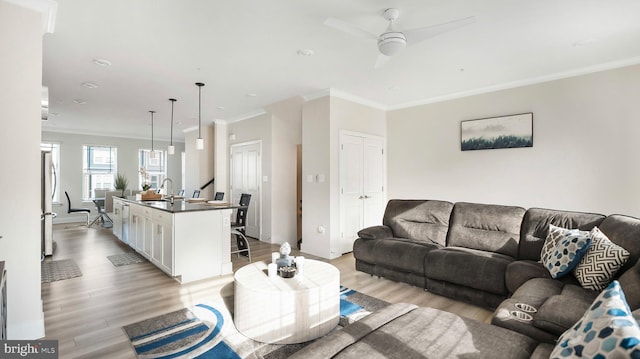 living room featuring baseboards, a ceiling fan, light wood-style flooring, and crown molding