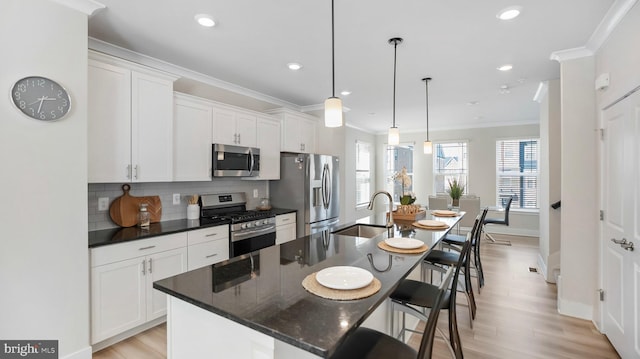 kitchen featuring a breakfast bar area, a kitchen island with sink, stainless steel appliances, a sink, and ornamental molding