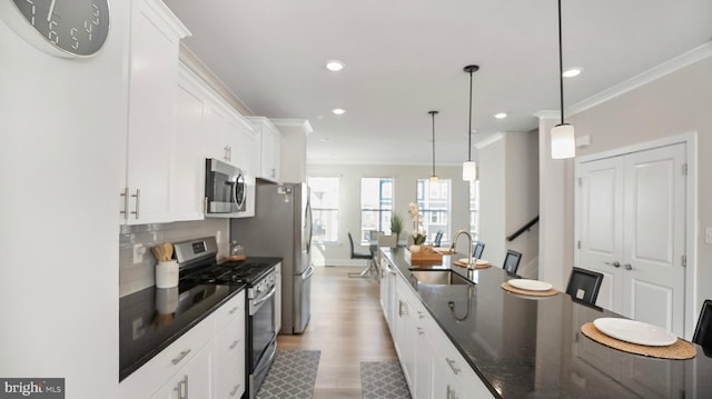 kitchen with white cabinets, dark countertops, appliances with stainless steel finishes, ornamental molding, and a sink