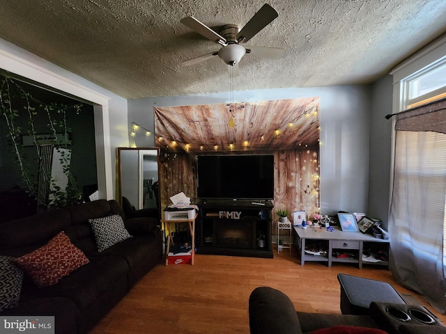 living room featuring a textured ceiling, a fireplace, wood finished floors, and a ceiling fan