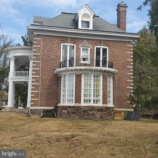 view of side of property featuring a yard, a balcony, and brick siding