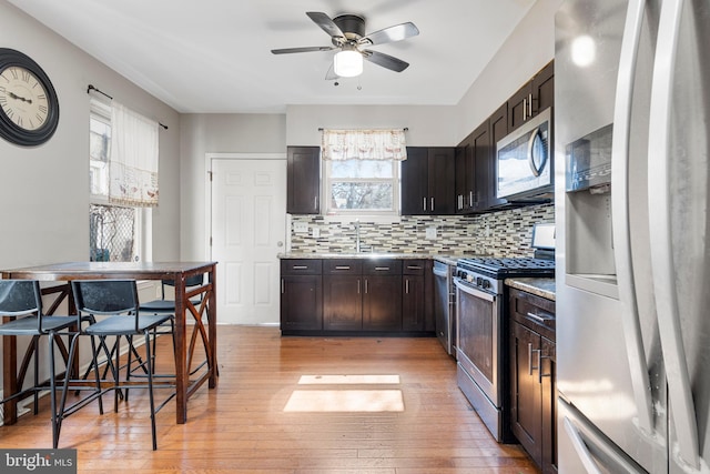 kitchen with light wood-style floors, light countertops, appliances with stainless steel finishes, dark brown cabinets, and backsplash