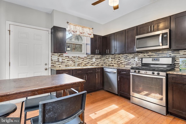 kitchen with appliances with stainless steel finishes, light wood-style floors, backsplash, and dark brown cabinets