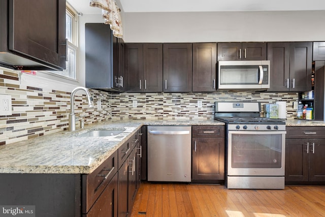 kitchen featuring stainless steel appliances, a sink, light wood-style flooring, and dark brown cabinets