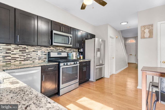 kitchen with stainless steel appliances, light wood-style floors, backsplash, and light stone countertops