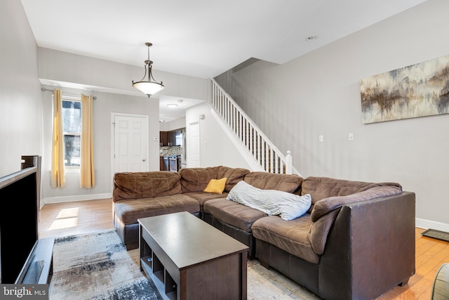 living room featuring stairs, baseboards, and light wood-style floors